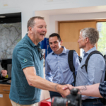 Group of 5 white men, two shaking hands, smiling and meeting