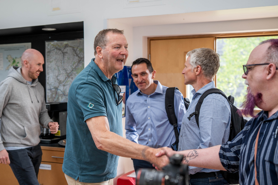 Group of 5 white men, two shaking hands, smiling and meeting