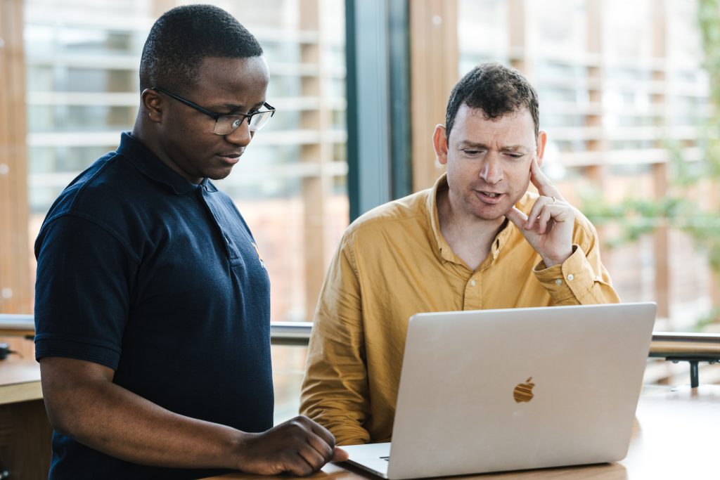 Two people at laptop - one black man standing and one white man sitting