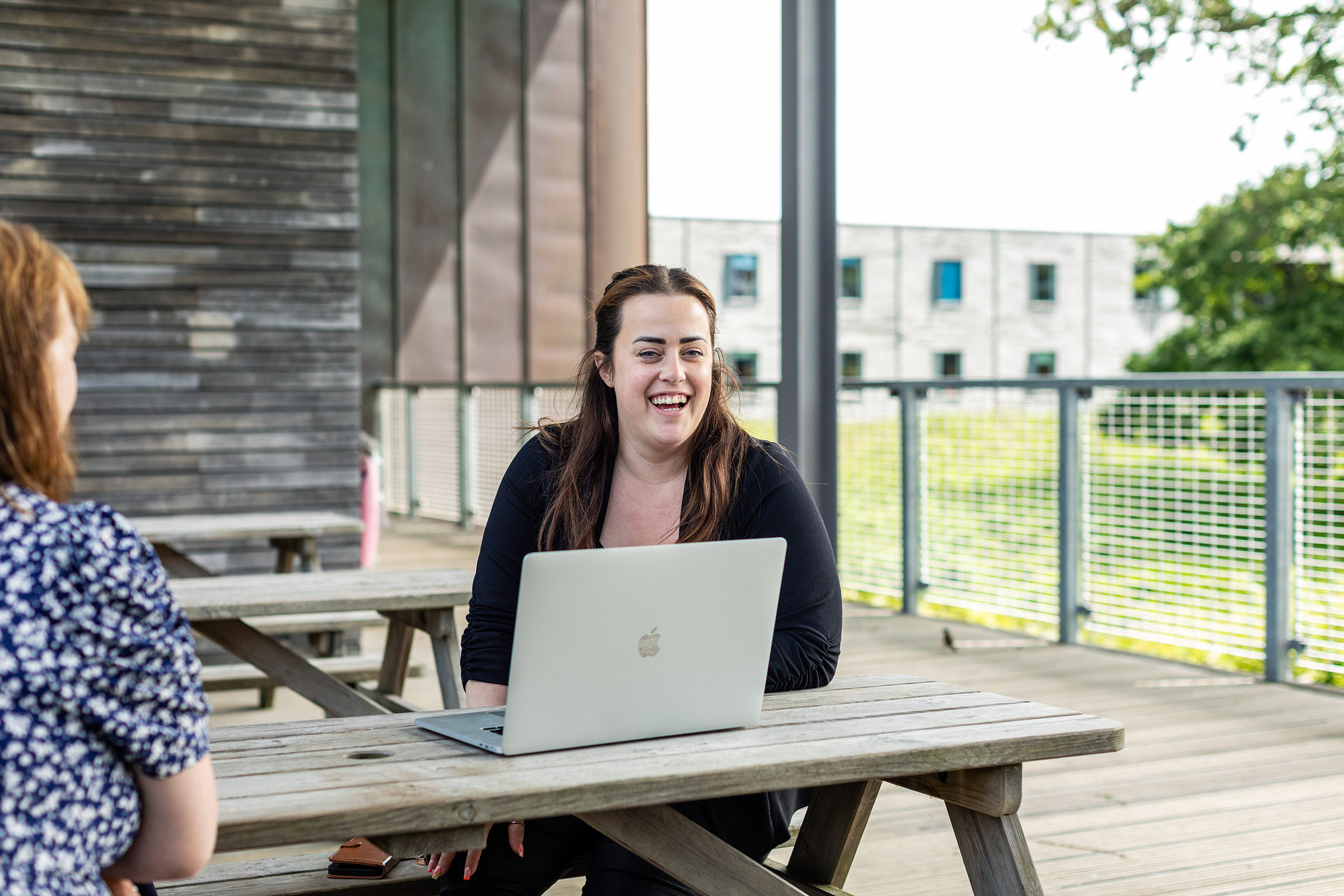 One woman working outside at laptop laughing