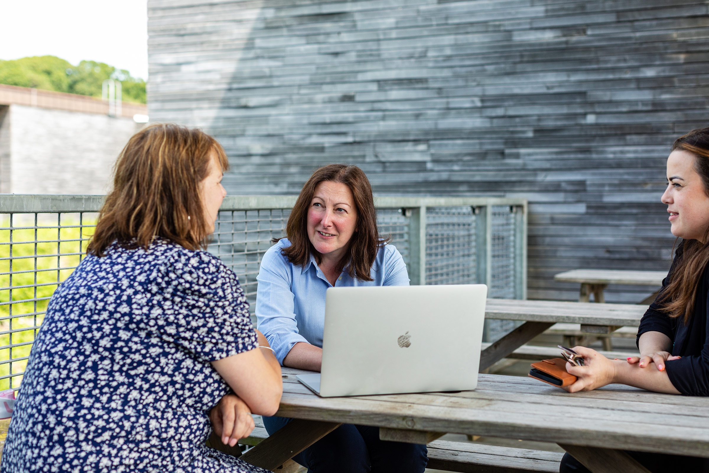 Three women at laptop working outside smiling