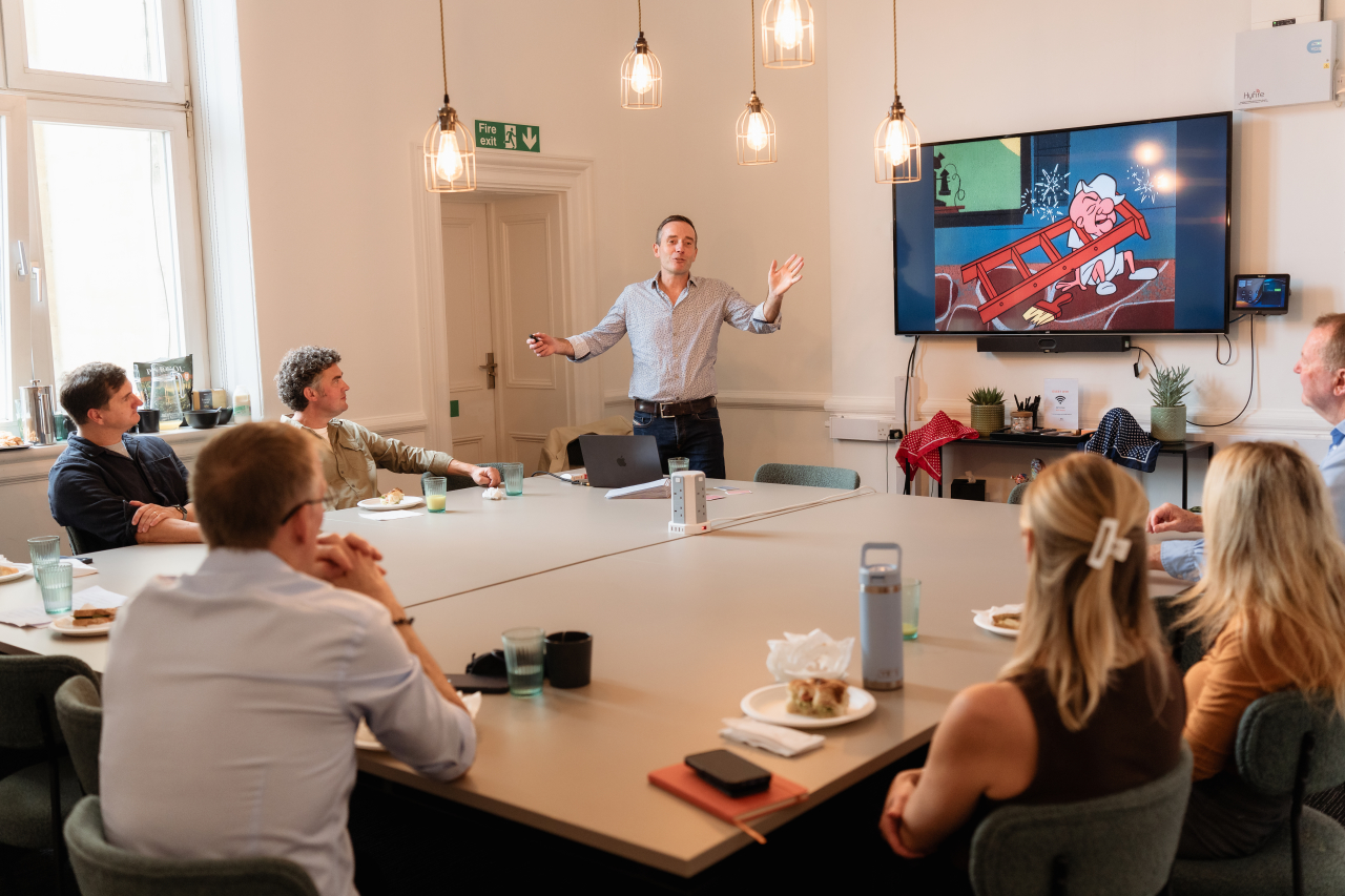 Man presenting to a room of people around a square table - relaxed but professional setting